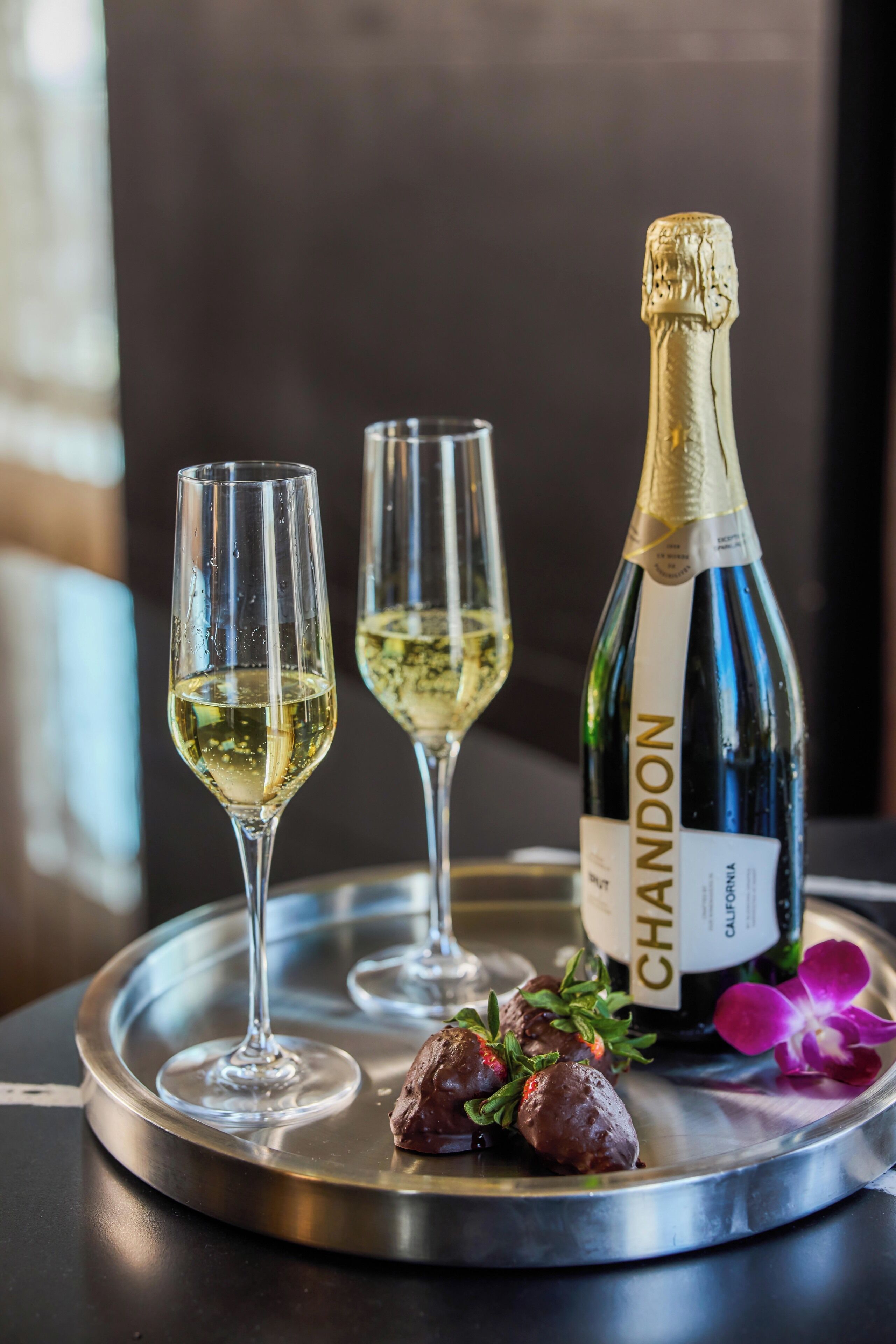 A bottle of Chandon champagne, two glasses, and a metal tray with a flower.