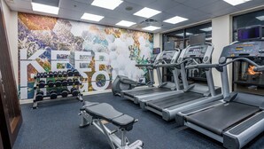 Un gimnasio con cintas de correr, pesas y un mural en la pared.