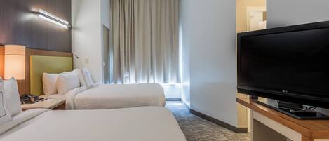 Une chambre d’hôtel avec deux lits, un téléviseur à écran plat, une table de chevet et une fenêtre avec des rideaux.