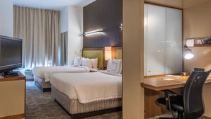 Habitación de hotel con dos camas, un escritorio, una silla, un televisor y un espejo grande.