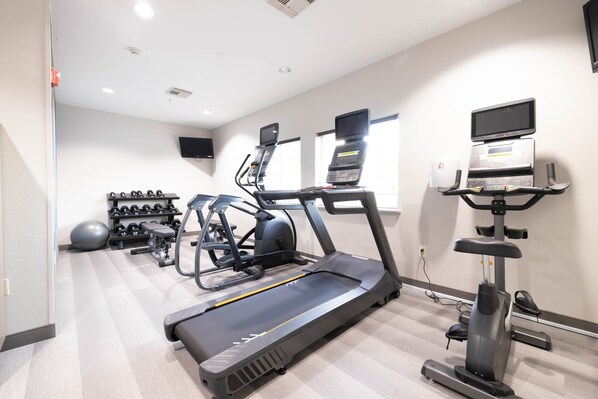Un gimnasio con cintas de correr, elípticas y equipamiento para levantamiento de pesas.