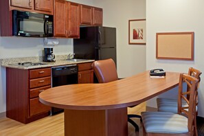 A kitchen with wooden cabinets, a microwave, a refrigerator, a coffee maker, and a dining table with chairs. - Candlewood Suites Houston Westchase/ Westheimer. by IHG (Houston)
