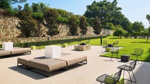 An outdoor seating area with lounge chairs and tables, a stone wall, and a well-maintained lawn. - Aloft by Marriott Las Colinas (Irving)