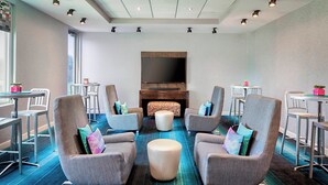 A modern lounge area with comfortable seating, a flat-screen TV, and a fireplace. - Aloft by Marriott Las Colinas (Irving)