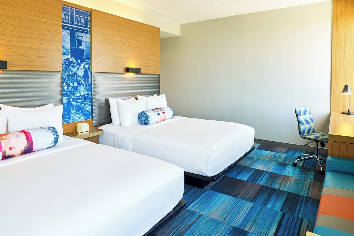 Habitación de hotel con dos camas, un papel tapiz azul con diseño, una alfombra azul y una silla.