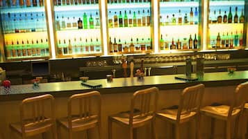 A bar area with multiple shelves of bottles, a neon sign, and bar stools.