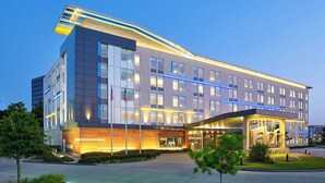 A modern hotel with a curved facade, large windows, and a covered entrance area. - Aloft by Marriott Las Colinas (Irving)