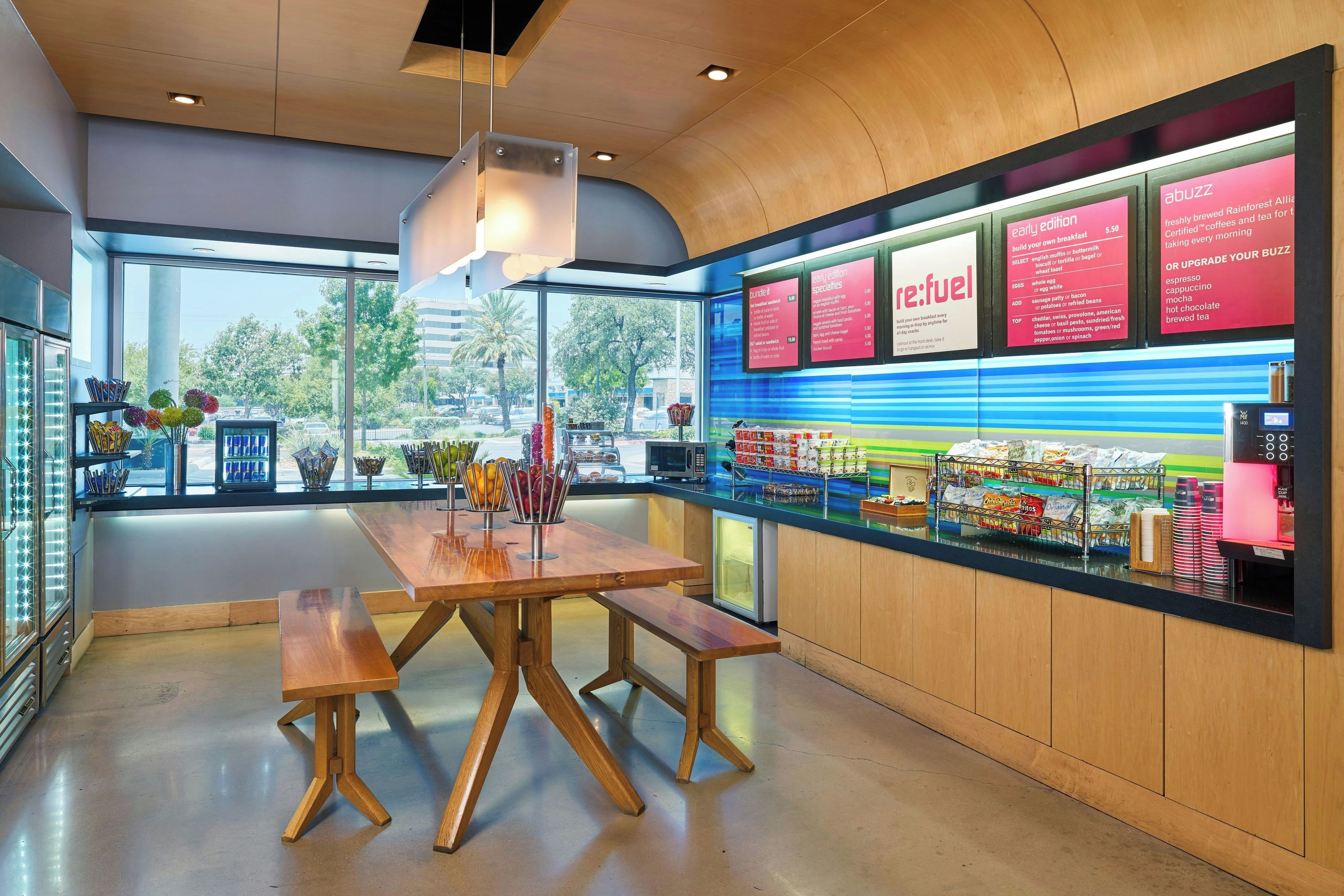 A café interior with a wooden table and benches, a menu board, and a view of the street outside.