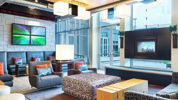 Un moderno hall de hotel con una zona de estar, televisor de pantalla plana, chimenea y ventanas amplias.