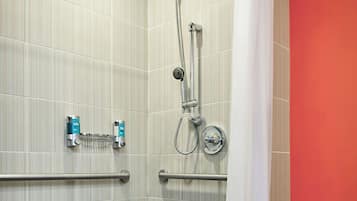 Un baño moderno con ducha, barras de apoyo y un secador de manos.