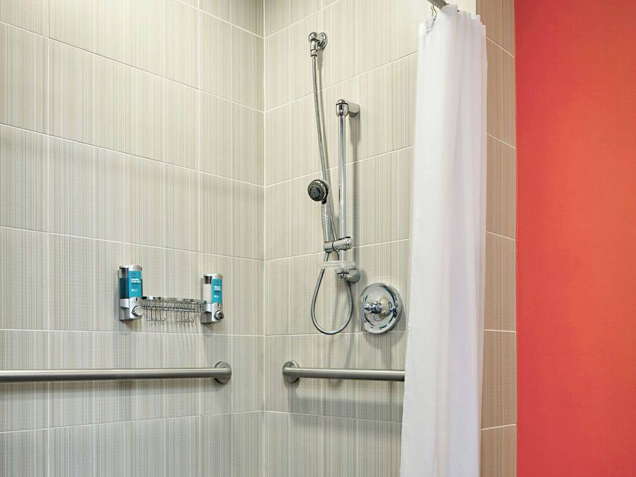 Un baño moderno con ducha, barras de apoyo y un secador de manos.