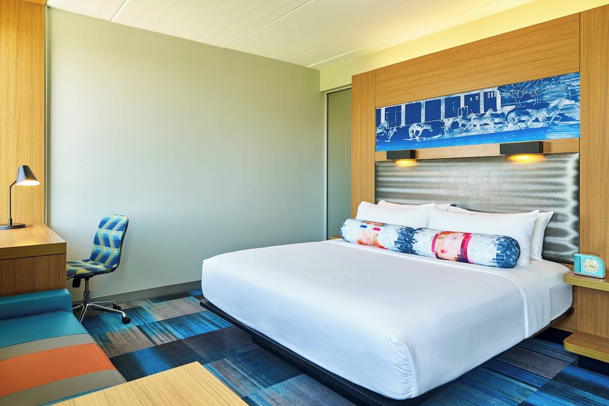 Una habitación de hotel con una cama grande, un escritorio, una silla y un cuadro en la pared.