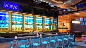 A bar area with a neon sign, multiple shelves of bottles, and bar stools. - Aloft by Marriott Las Colinas (Irving)