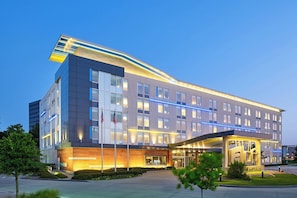 A modern hotel with a prominent entrance, multiple floors, and a unique architectural design. - Aloft by Marriott Las Colinas (Irving)