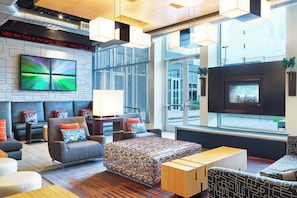 A modern hotel lobby with a seating area, a fireplace, and a large TV screen. - Aloft by Marriott Plano (Plano)