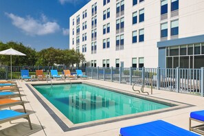 A swimming pool with lounge chairs and a building with multiple windows.