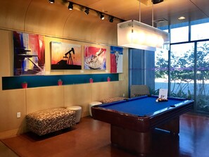 A pool table with a blue felt surface, a sofa, a bench, and two potted plants on a wooden floor. - Aloft by Marriott Plano (Plano)