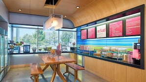 Una cafetería moderna con interior de madera, un ventanal grande y un cartel con diferentes opciones de café.