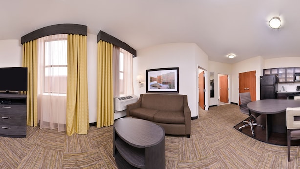 A hotel room with a TV, sofa, armchair, dining table, and kitchen area.