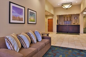 A hotel lobby with a reception desk, a sofa with striped cushions, and framed pictures on the wall.