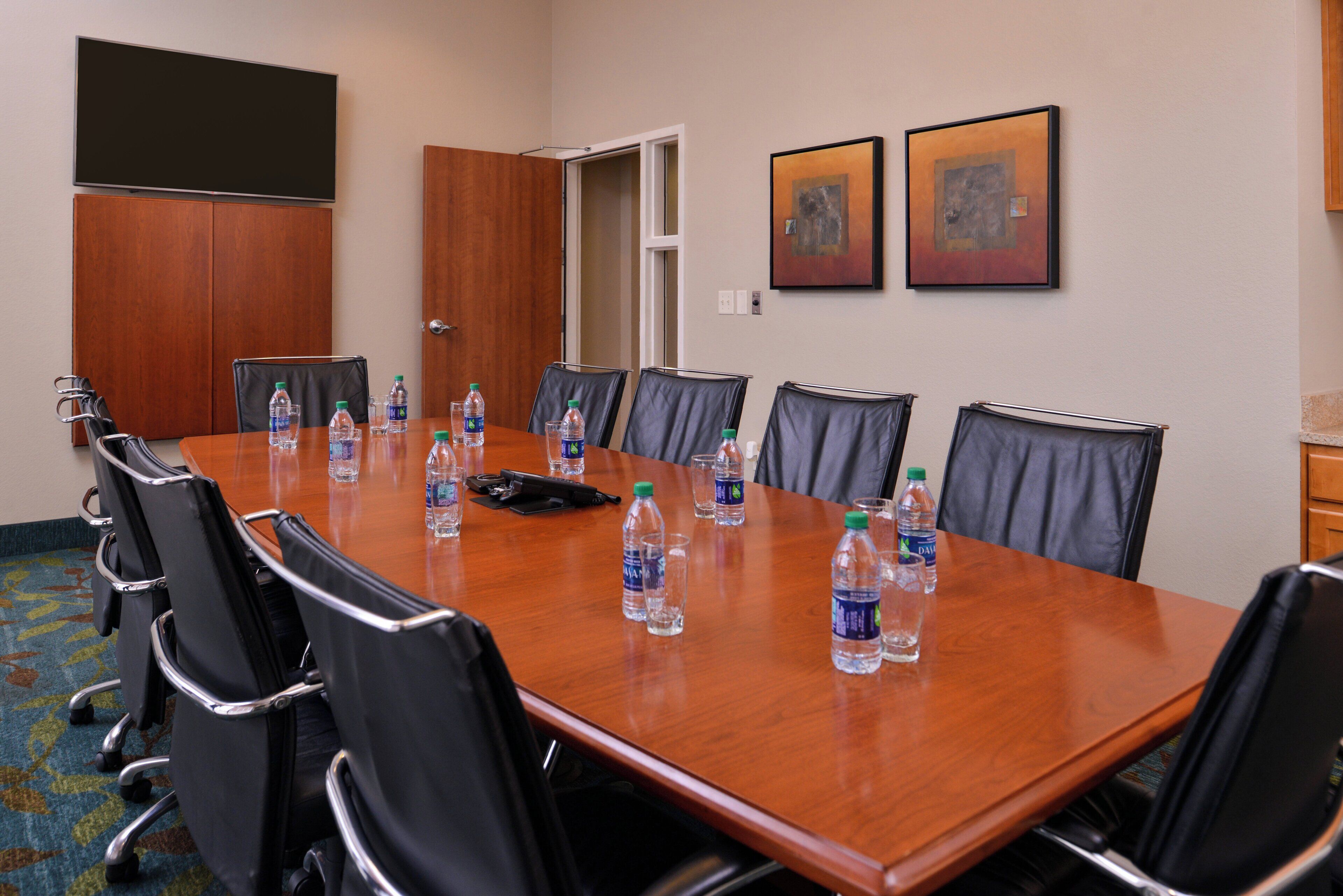 Un salón de conferencias con una larga mesa, sillas negras y botellas de agua.