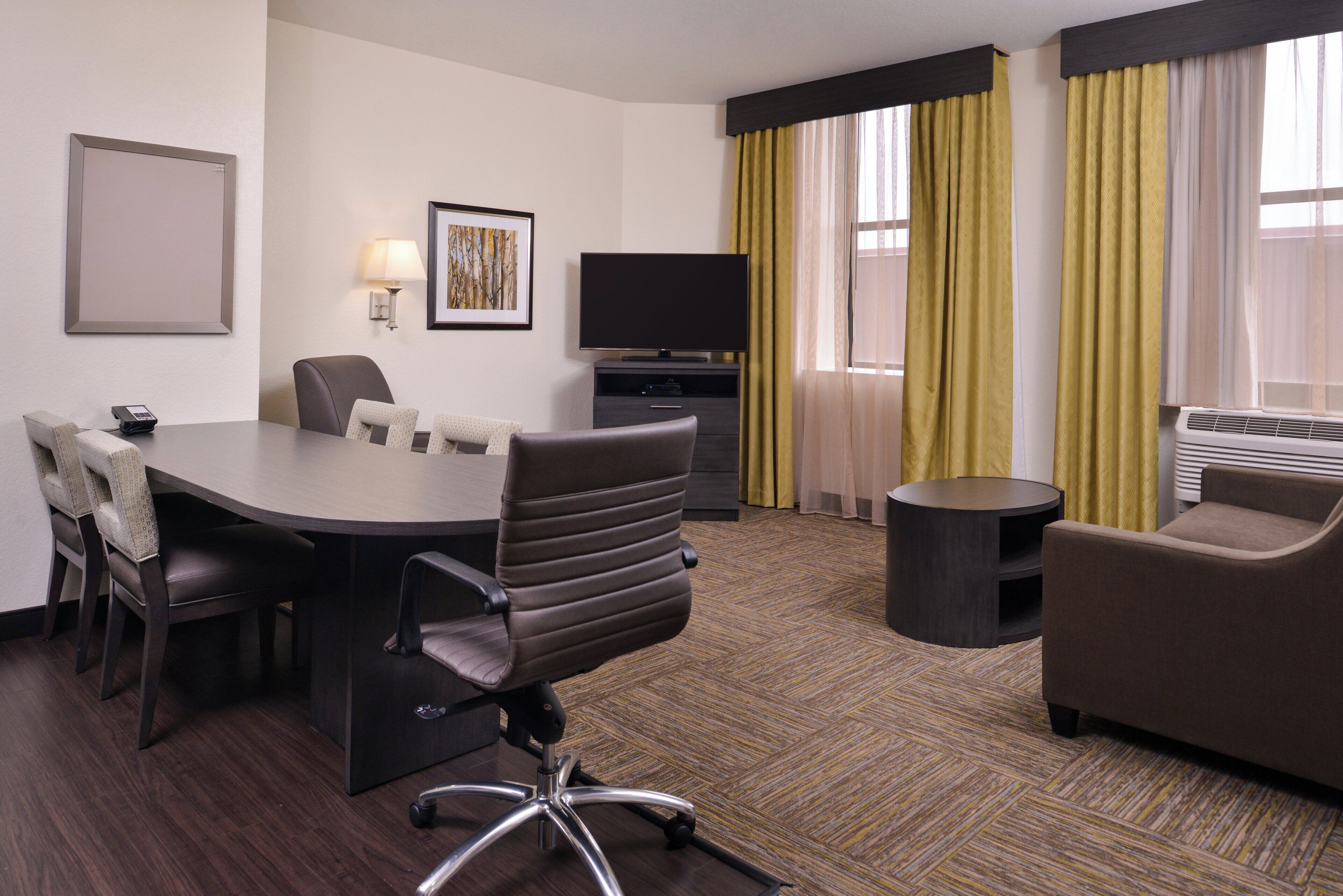 A hotel room with a conference table, chairs, a television, a sofa, and a small side table.