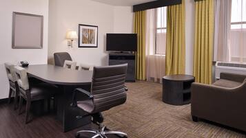 A hotel room with a conference table, chairs, a television, a sofa, and a small side table.