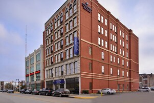A multi-story hotel with a prominent 'CANDLEWOOD SUITES' sign, a classic architectural style with a brick facade, and a corner location with street parking.