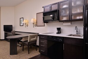 Quarto de hotel compacto com cozinha compacta, incluindo micro-ondas, cafeteira e pia. Há uma mesa com cadeira e televisão de tela plana.