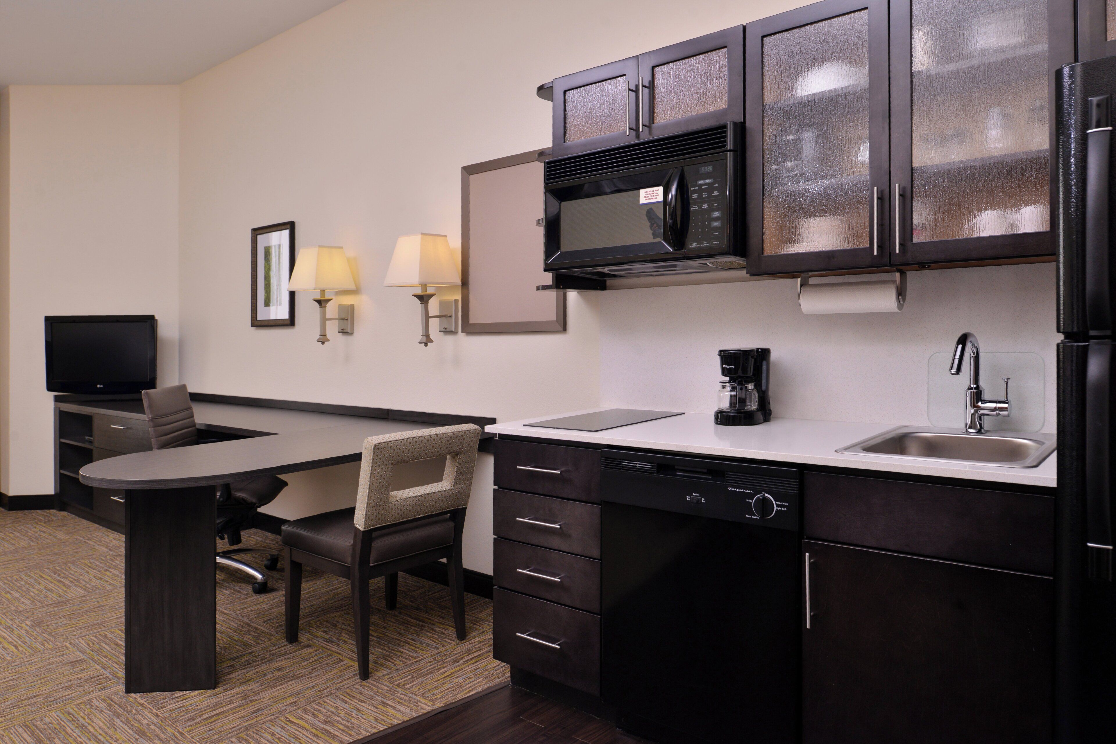 Habitación de hotel compacta con kitchenette, comedor y televisor.