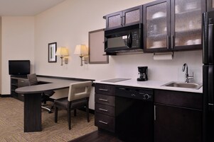 A compact hotel room with a kitchenette, a dining area, and a television.