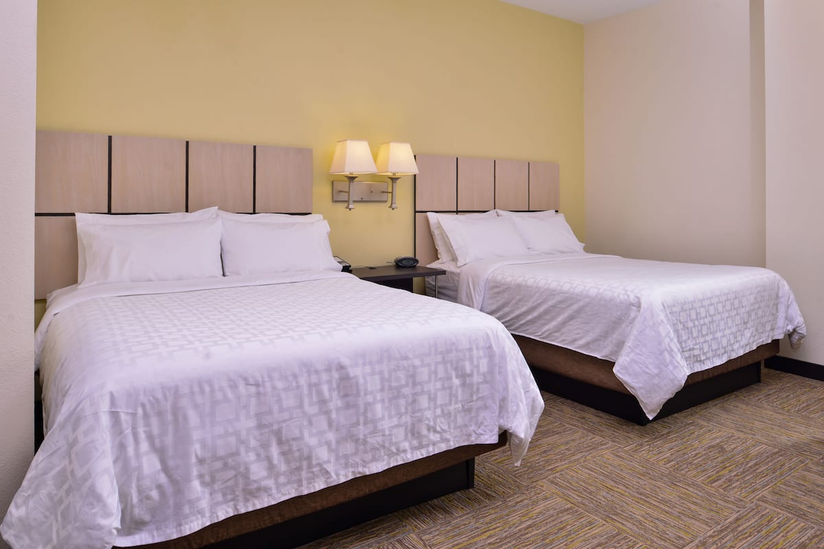 Une chambre d’hôtel avec deux lits, une table de chevet avec une lampe et un luminaire fixé au mur.