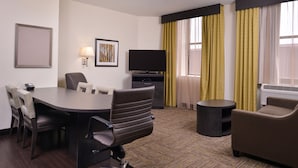 A hotel room with a conference table, chairs, a television, a sofa, and a small side table.
