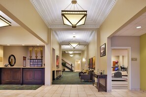 Un hall d’hôtel comprenant un comptoir d’accueil, un escalier et un espace dédié à la salle de sport.