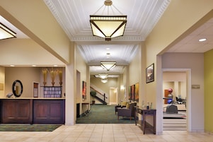 A hotel lobby with a reception desk, a staircase, and a gym area.