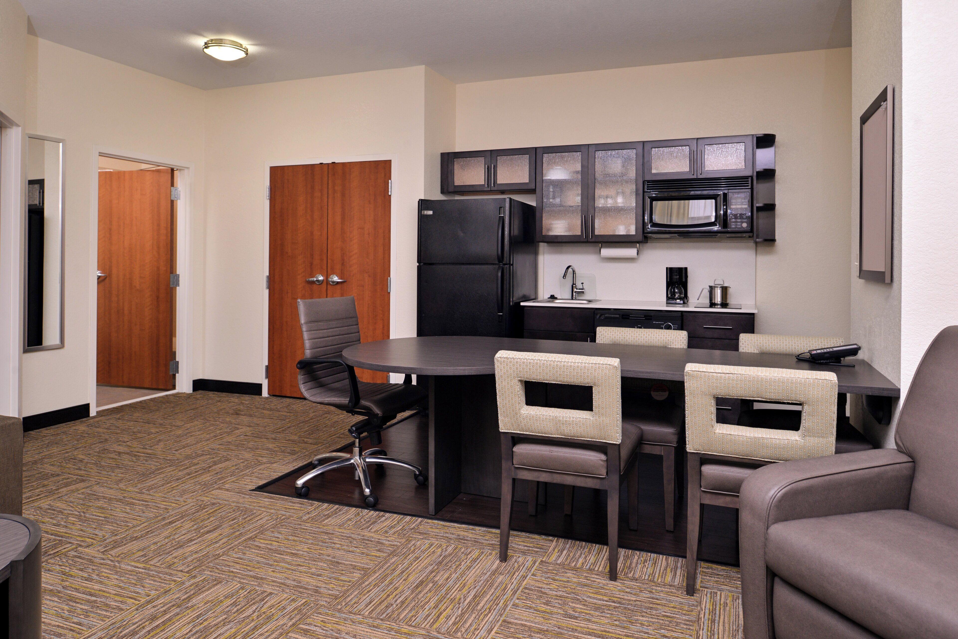 A compact kitchen with a refrigerator, microwave, and sink. There is a dining table with four chairs.