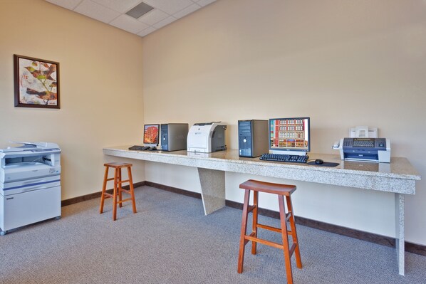 A workspace with a long desk, multiple computers, a printer, and two wooden stools.