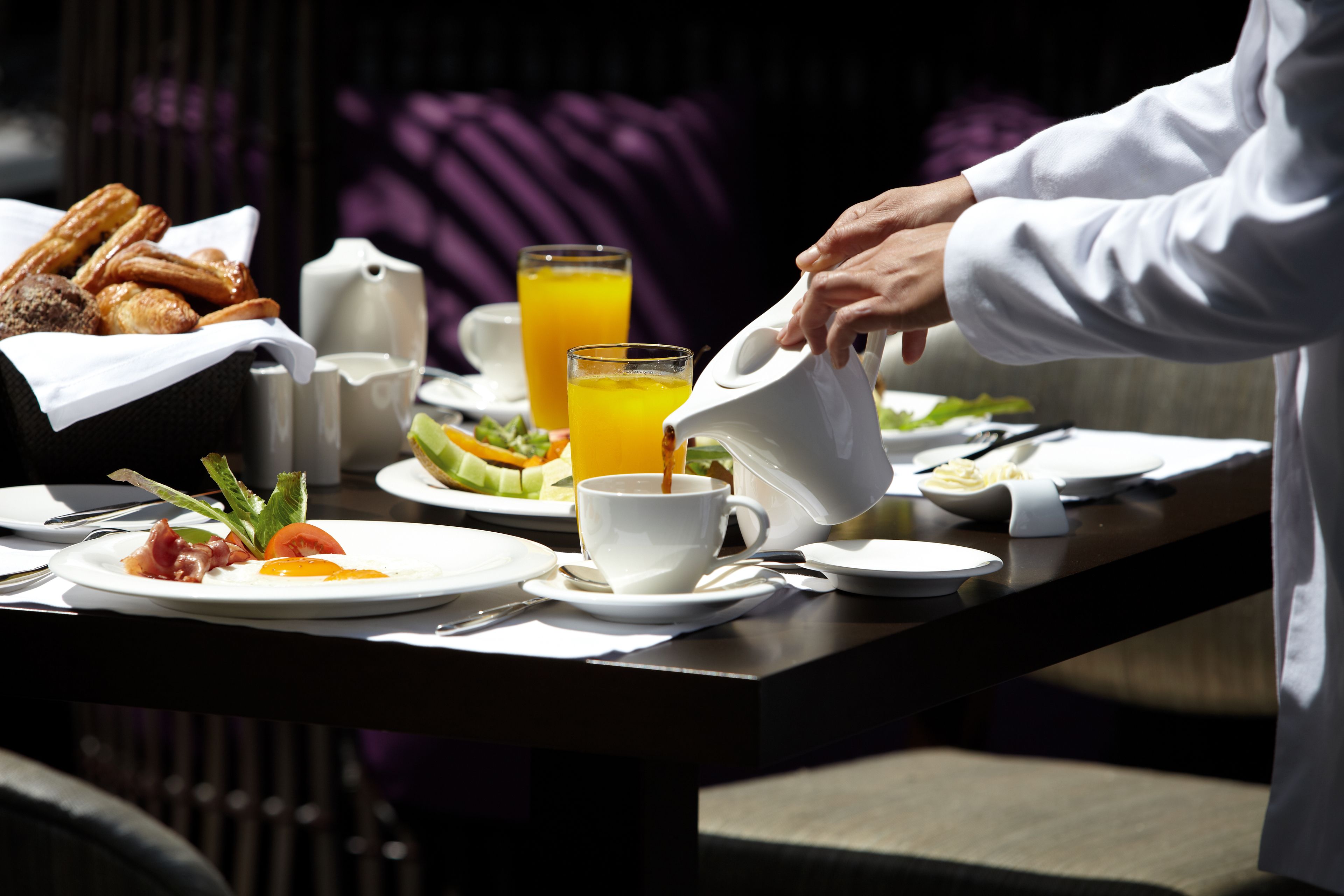 A breakfast table with croissants, a pitcher of orange juice, and a cup of coffee.