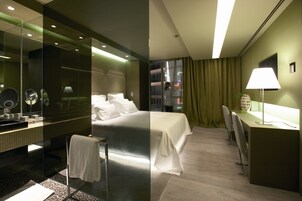 A hotel room with a large bed, a desk with a lamp, a mirror, and a view of the outside.