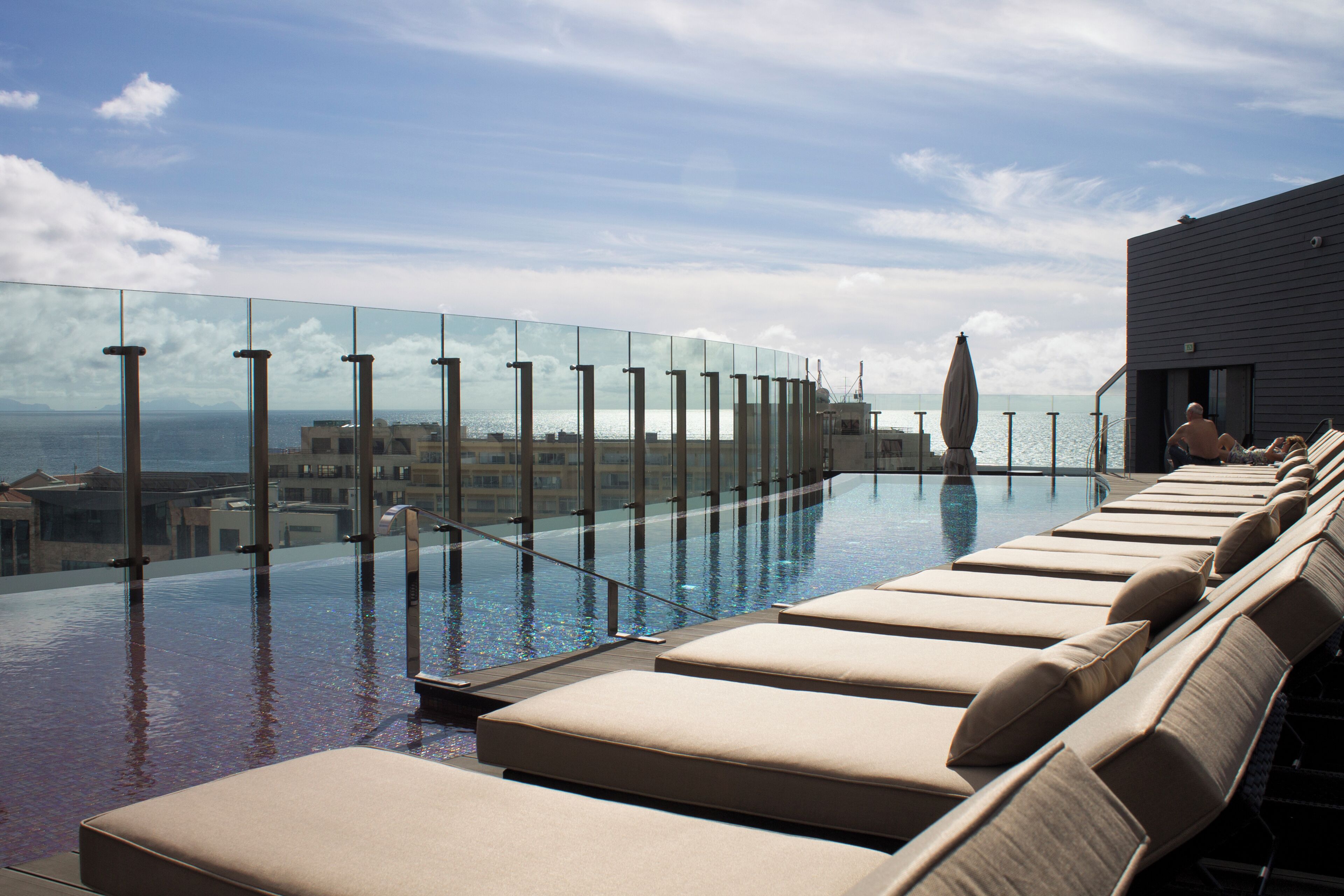 An infinity pool with lounge chairs and a glass barrier overlooking the sea.