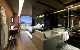 A modern hotel room with a large bed, a separate bathroom with a bathtub, a desk, and a chair.