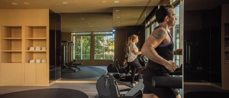 A gym with exercise equipment, large windows, and a mirrored wall.