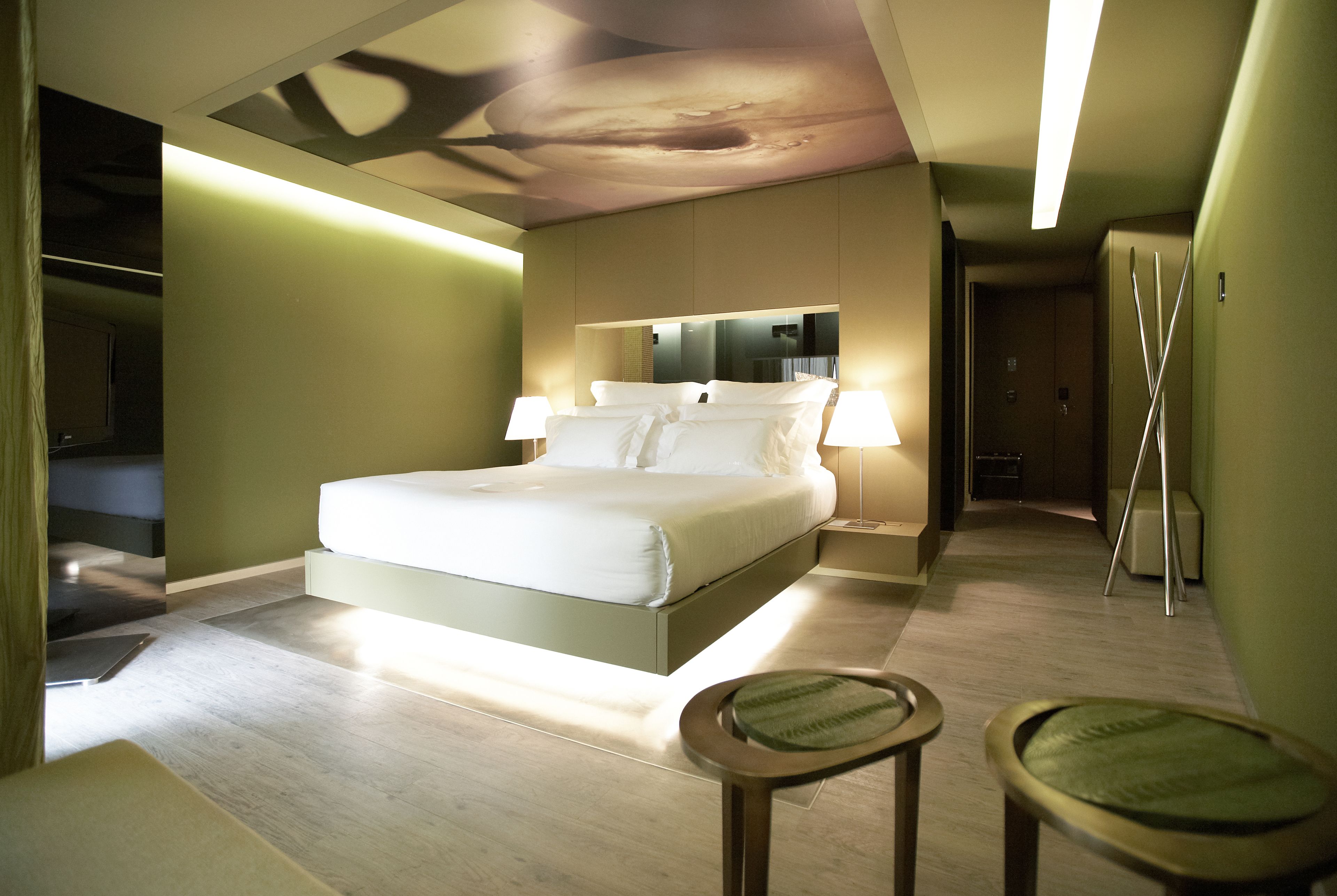 A modern bedroom with a large bed, bedside lamps, and a mirror above the bed.