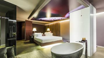 Una habitación de hotel moderna con una cama grande, un baño independiente con una bañera de pie y un mural en el techo.