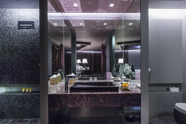 Un baño moderno con un espejo grande, una bañera negra y una zona de tocador con azulejos.