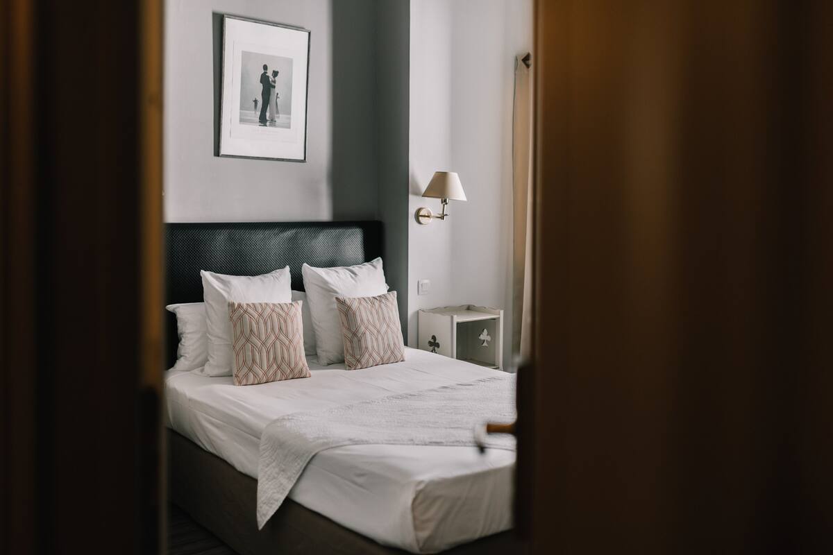 A neatly made bed with white and patterned pillows, a framed picture on the wall, and a bedside lamp.