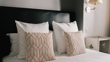 A neatly made bed with white linens and two patterned pillows, a black headboard, and a wall-mounted lamp.