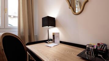 Une chambre d’hôtel avec un bureau en bois, une lampe noire, un miroir et un plateau avec des chocolats.