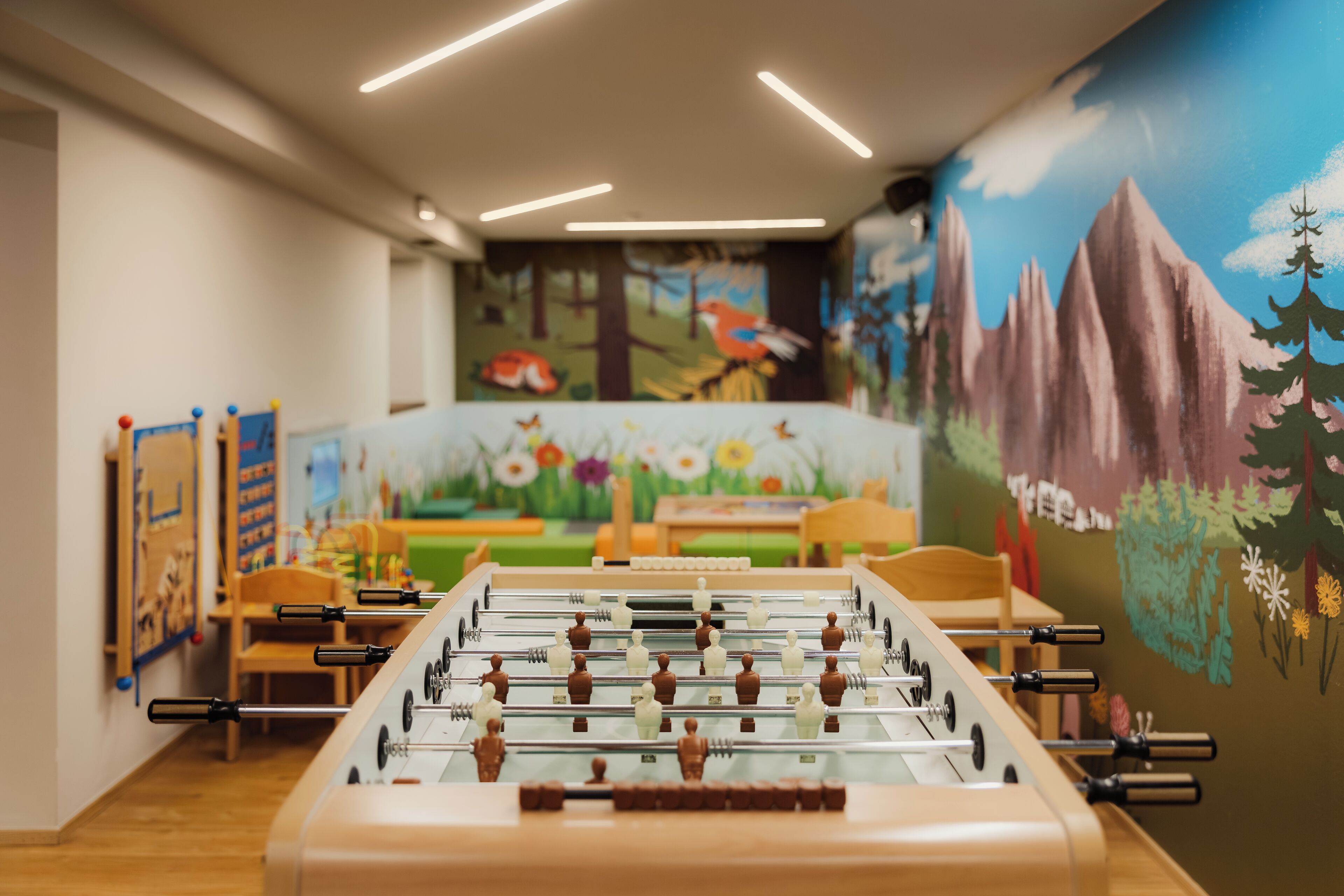 A foosball table in a room with a mural of a forest and mountains on the wall.