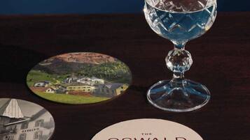 Un vaso de agua, un posavasos con el texto 'OSWALD GRAND HOTEL' y dos posavasos circulares con imágenes de edificios.